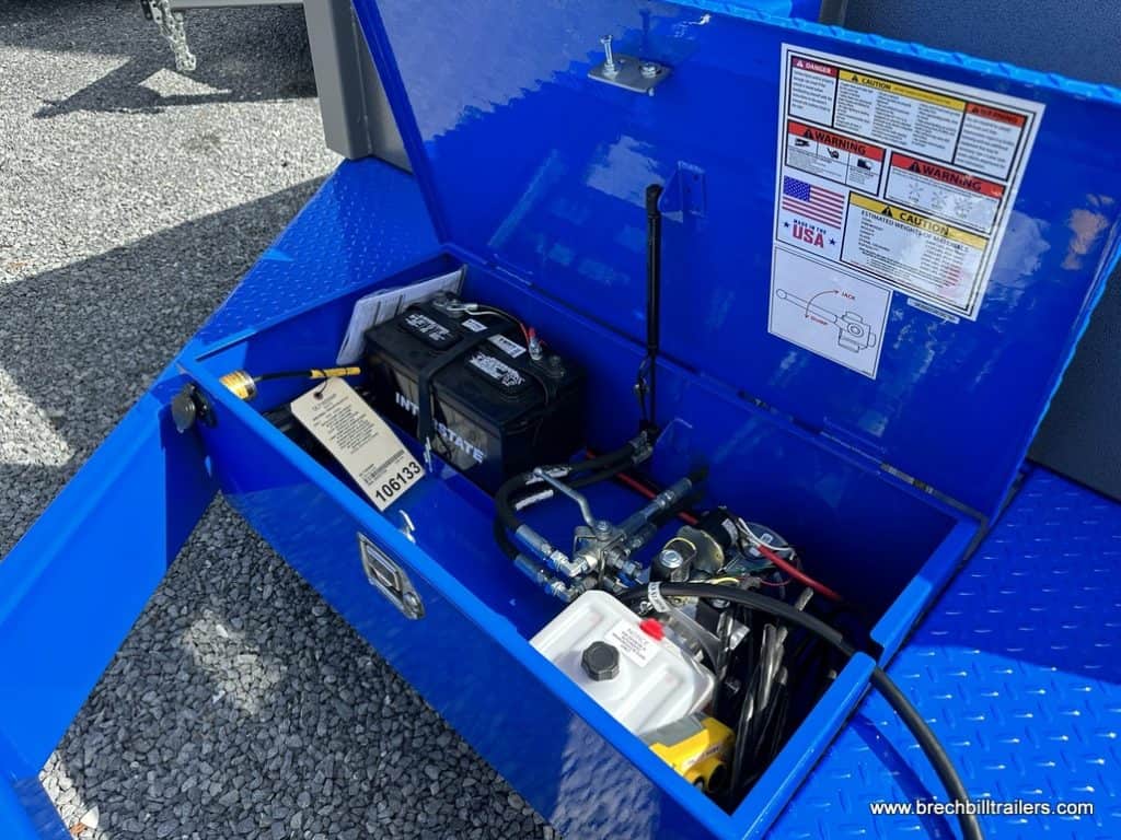 Blue storage box with battery, hydraulic lines and fluid reservoir.